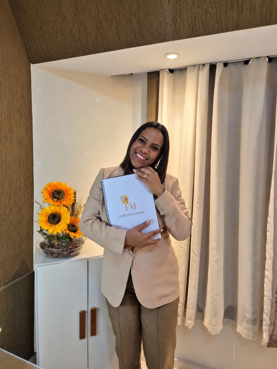 Danielle Casemiro segurando o Caderno FEM no consultório, ao lado de girassóis